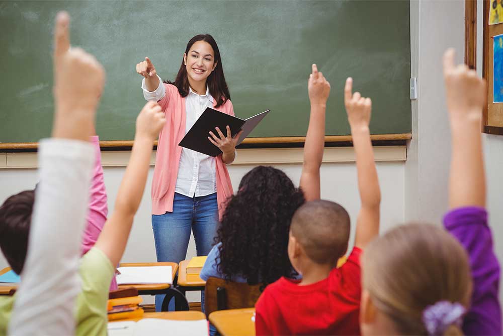 teacher in classroom children with hands up